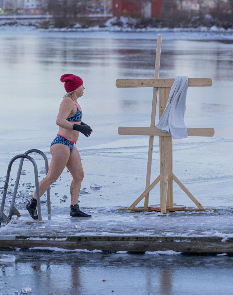 Woman in bikini walking on frozen boardwalk by icy lake during winter.
